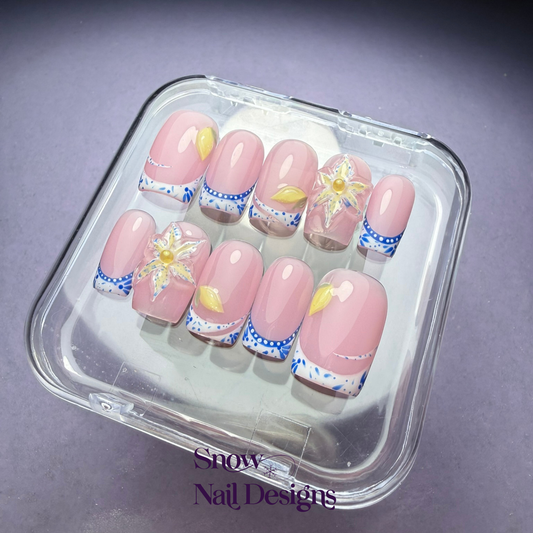 Flatlay foto van handgemaakte press-on nagels met blauwe Franse tips, gele accenten en 3D bloem met parel – Porto Petal van Snow Nail Designs