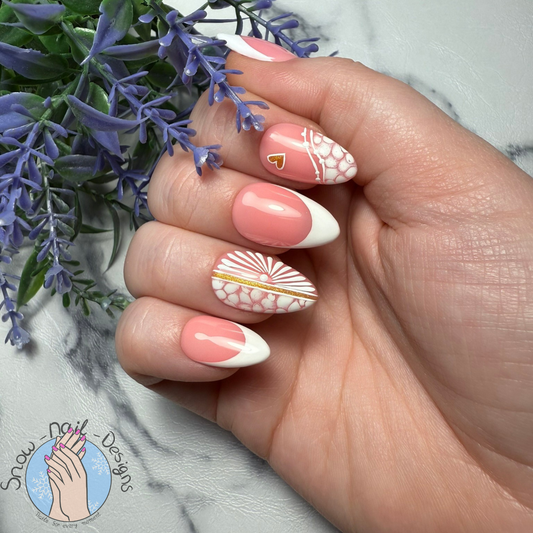 Hand met Sunset Glow press-on nagels in koraalroze en wit, versierd met gouden details en patronen.