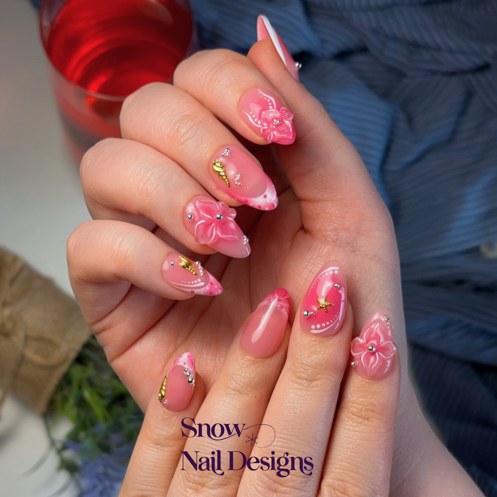 Handgemaakte roze press-on nagels gedragen aan de hand met 3D bloemen, gouden zeester en schelp – Pink Shore van Snow Nail Designs