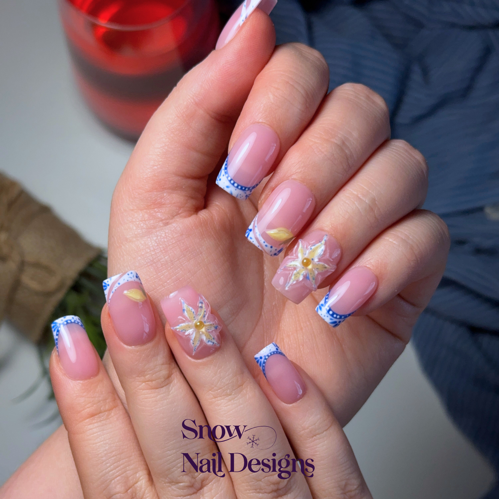 Handgemaakte press-on nagels gedragen aan de hand met blauwe Franse tips, handgeschilderde patronen en 3D bloem – Porto Petal van Snow Nail Designs