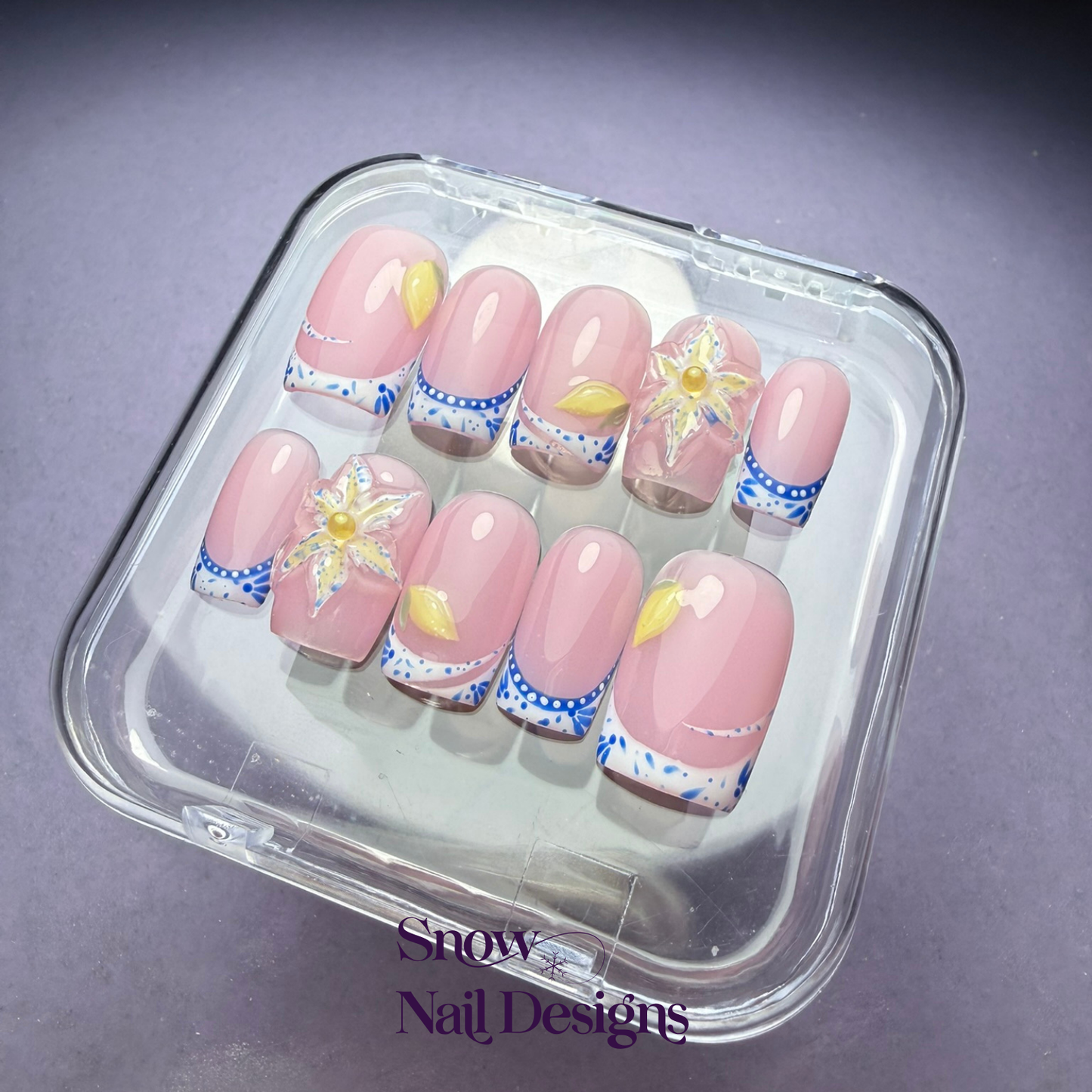 Flatlay foto van handgemaakte press-on nagels met blauwe Franse tips, gele accenten en 3D bloem met parel – Porto Petal van Snow Nail Designs