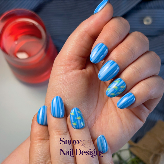 Handgemaakte blauwe press-on nagels gedragen aan de hand met licht blauwe strepen en citroentjes – Limone van Snow Nail Designs