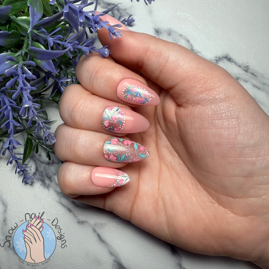 Nagelset met een rustige basis, roze cat eye en verfijnde bloemmotieven, gedragen op een hand.