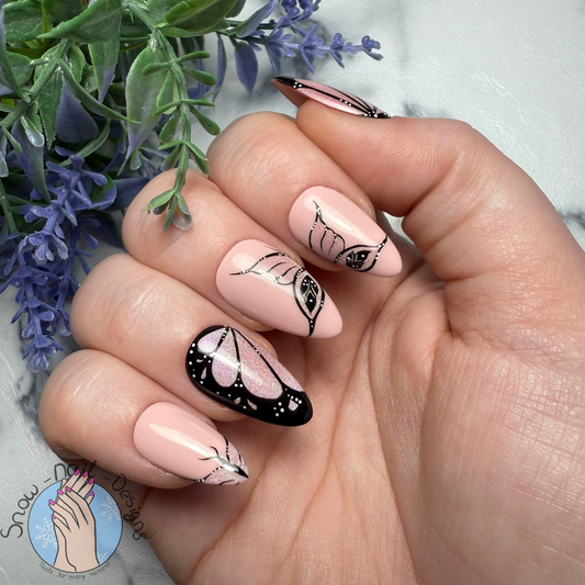 Hand met Celestial Wings press-on nagels in nude en holografisch roze met zwarte vlindervleugels.