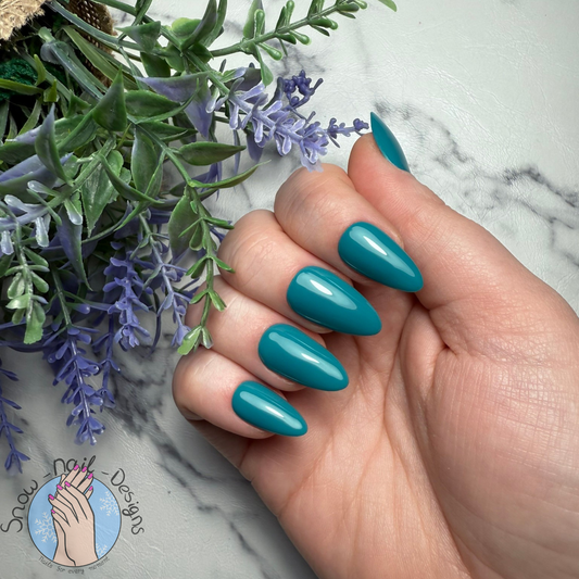 Hand met diepe teal press-on nagels in een stijlvolle, gedurfde kleur.