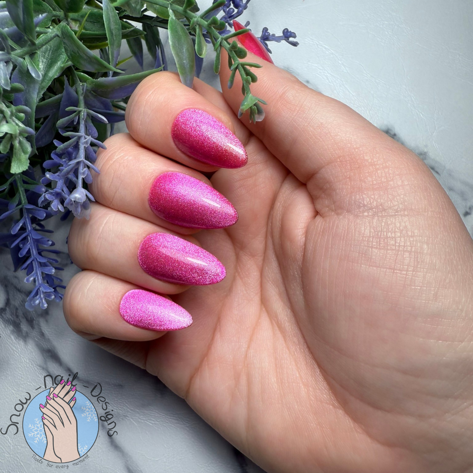 Hand met felroze press-on nagels met een sprankelend cat eye effect.
